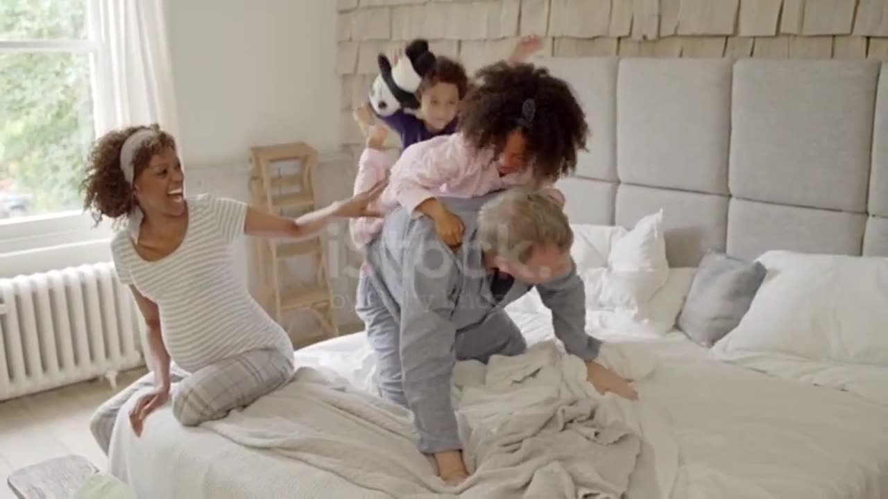 Multi-ethnic daughters jumping on father's back on bed