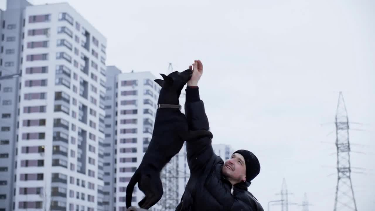 Man handler training black dog to stand on its hind legs on winter walk