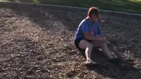 Slowmo blue shirt girl jumps off swingset and lands on knees