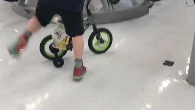 Kid rides a small green bike and falls back