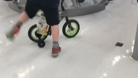 Kid rides a small green bike and falls back