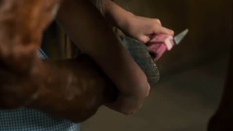 Unrecognizable girl using brush and pick to remove dirt from hoof of horse in stable