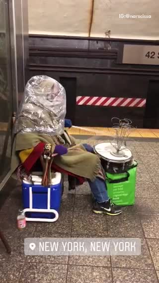 Person with plastic bag over their head plays drums in subway station