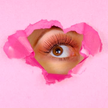Eye of a woman peeking out of the hole of a pink paper screen
