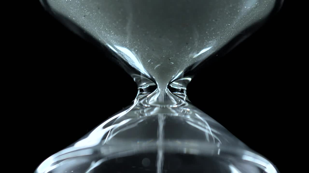Glass hourglass close up on a black background