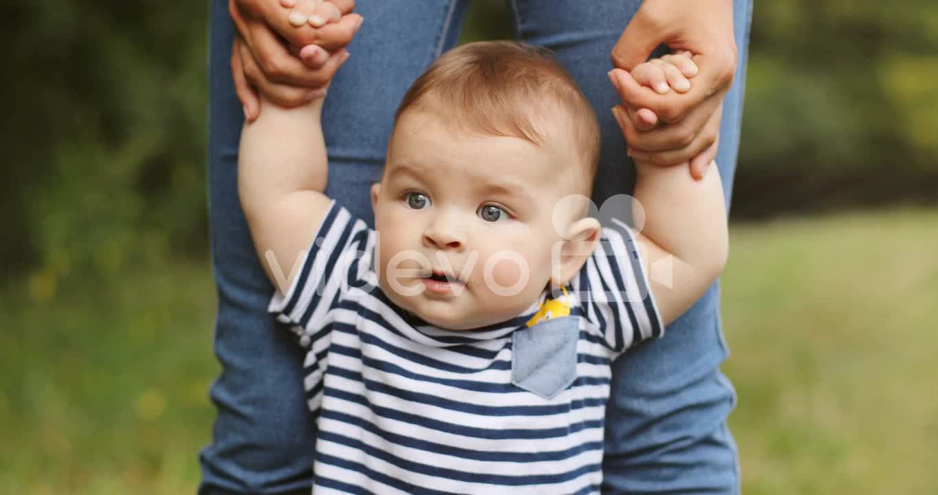 Close Up Of A Baby Boy Taking His First Steps In The Grass While Holding His Mother's Hands