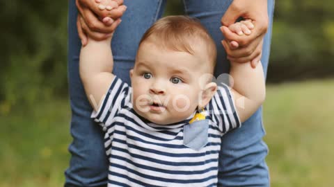 Close Up Of A Baby Boy Taking His First Steps In The Grass While Holding His Mother's Hands