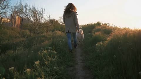 Young female running with retriever dog on sunny path at sunset