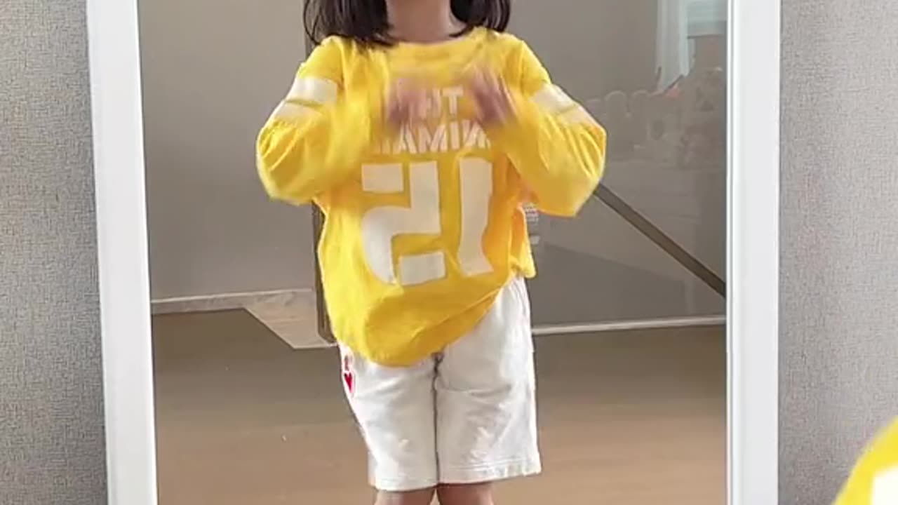 Little girl dancing in front of the mirror in yellow shirt