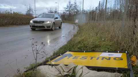 Wide Shot of Car Driving Past Fallen Over COVID 19 Test Site Road Sign