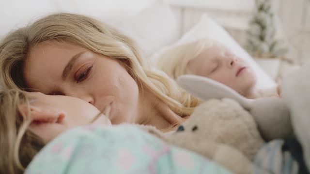 A Mother Loving Moments With Her Two Children Lying In Bed Together