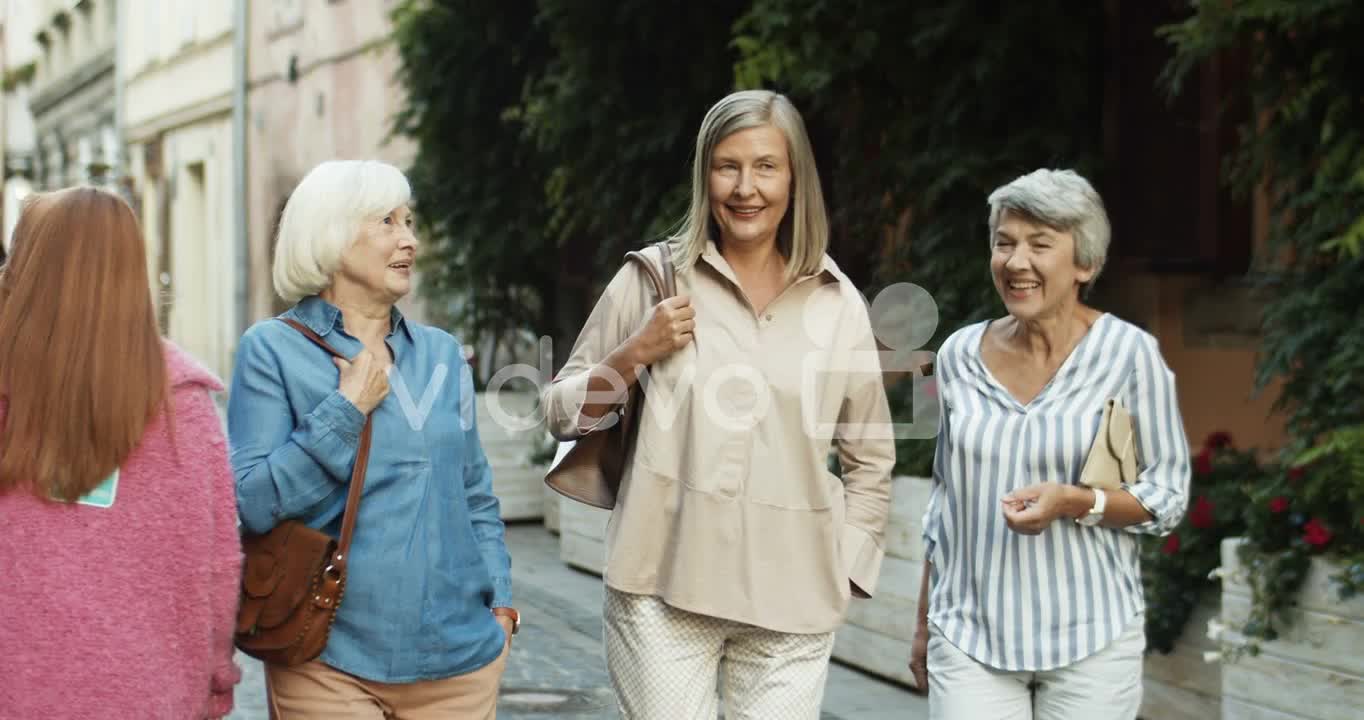 Three Cheerful Senior Women On Retirement Walking The Old City Street And Laughing While Talking