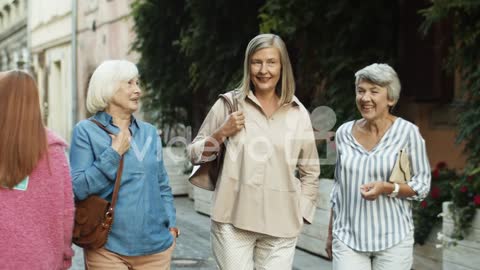 Three Cheerful Senior Women On Retirement Walking The Old City Street And Laughing While Talking