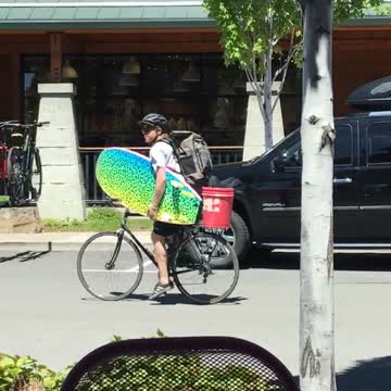Guy riding bike holding colorful blue yellow surfboard