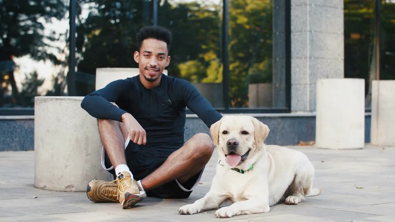 Portrait of young black man and his white labrador dog beside him in city center in the morning