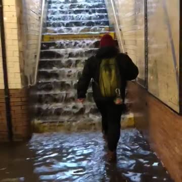 Person in red beanie walks up stairs with water running down