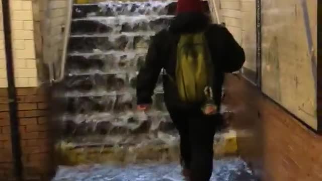 Person in red beanie walks up stairs with water running down