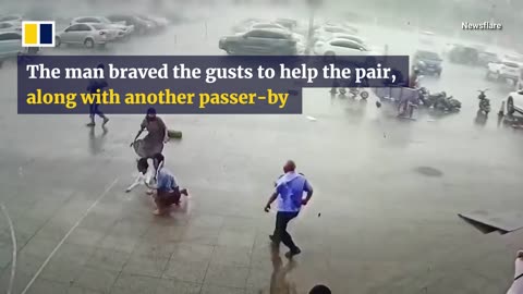 Security guard helps pedestrians knocked off feet in strong winds.mp4