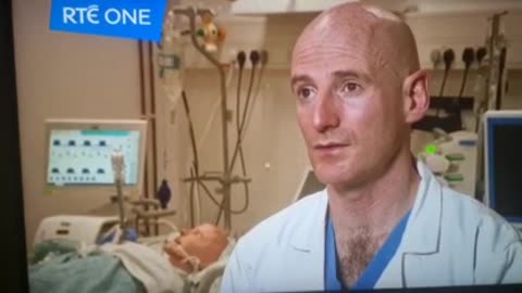 A dummy in the bed in the background as a doctor describes how overworked they are!