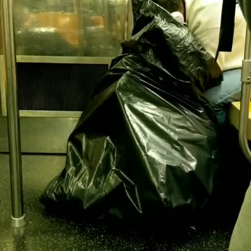 Person white headphones looking through big black trash bag