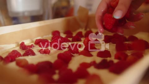 Woman adding a large quantity of raspberries to a sweet homemade dessert in a mold ready to cook