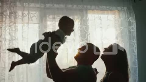 Silhouettes Of Loving Parents With A Child At The Window Of Their Apartment