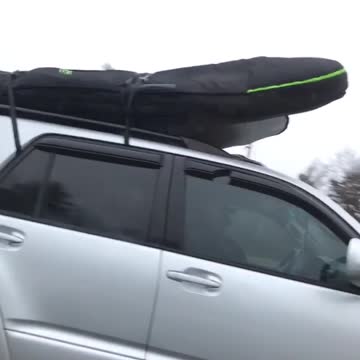 Silver car drives with surfboard on top of car