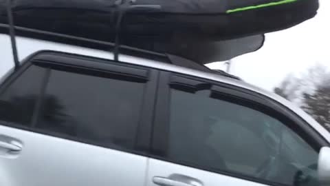 Silver car drives with surfboard on top of car