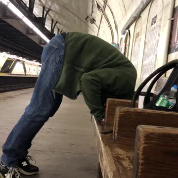 Guy blue jeans green jacket head in wooden seats standing subway