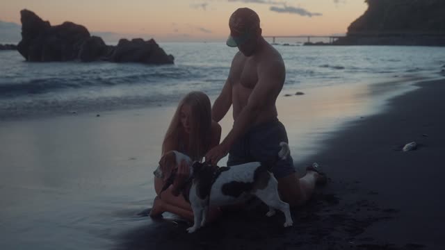 A couple petting their dog on the beach