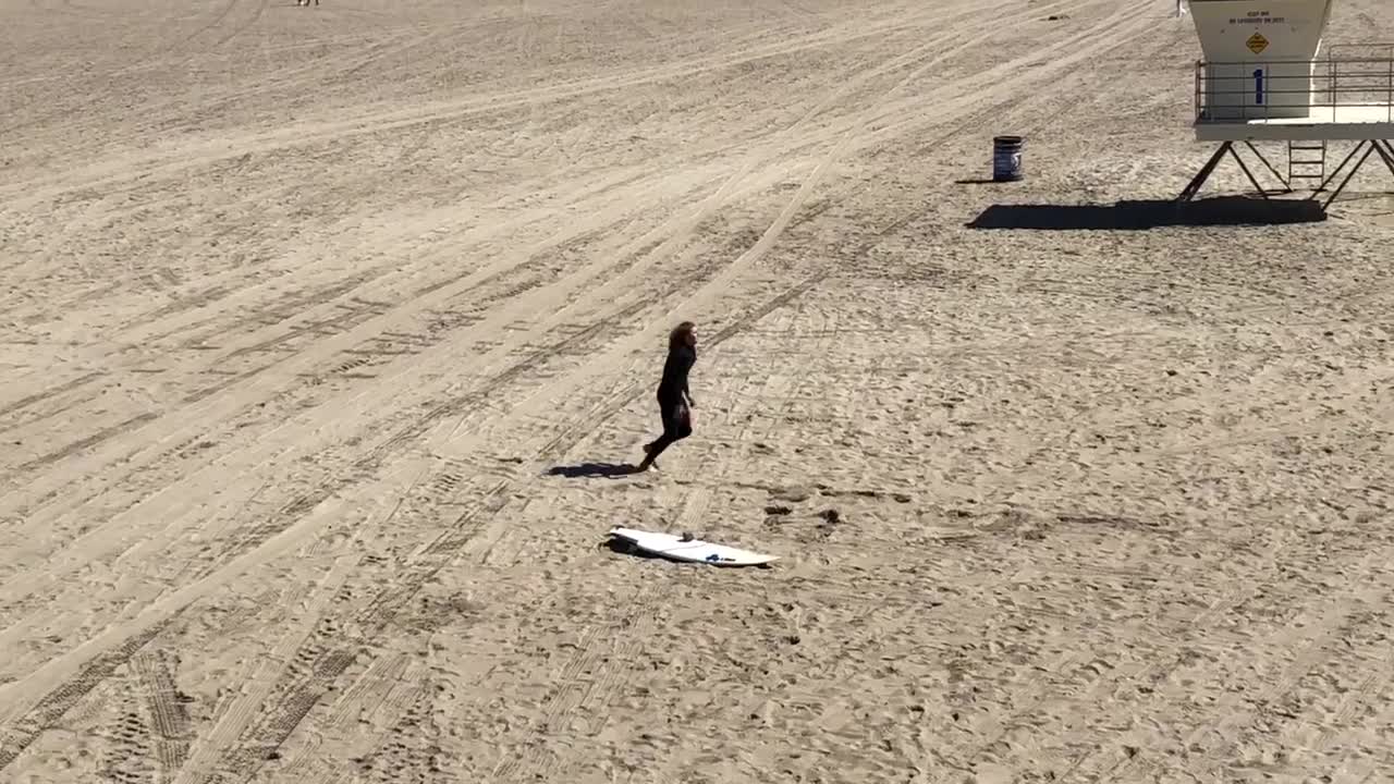 Guy in wetsuit does stretches on the beach next to surfboard