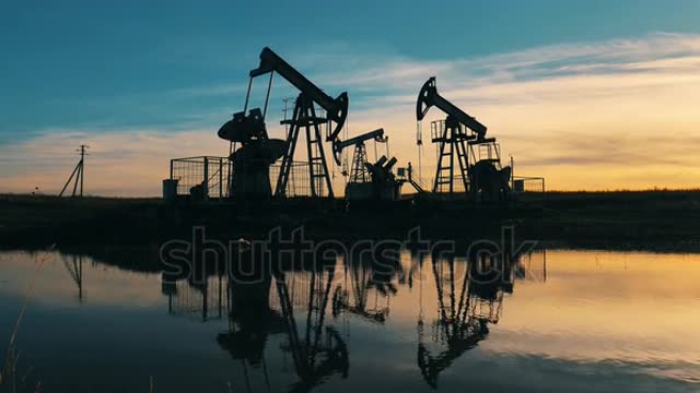 Oil pumping units operating at sunset, reflected on water surface