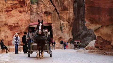 People and horse with carriage in narrow passage, red gorge that leads to Petra