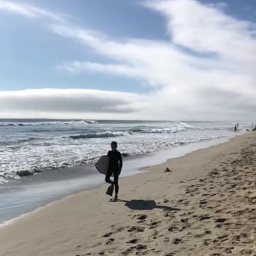 Boogie boarder walks down beach with flipper feet
