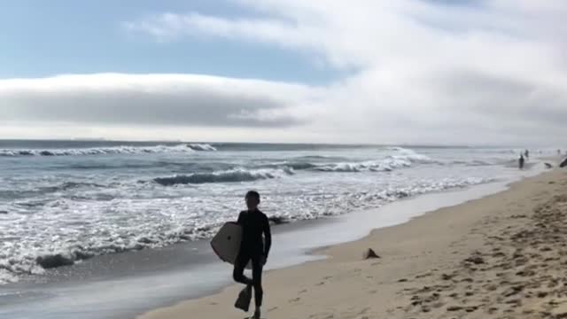 Boogie boarder walks down beach with flipper feet