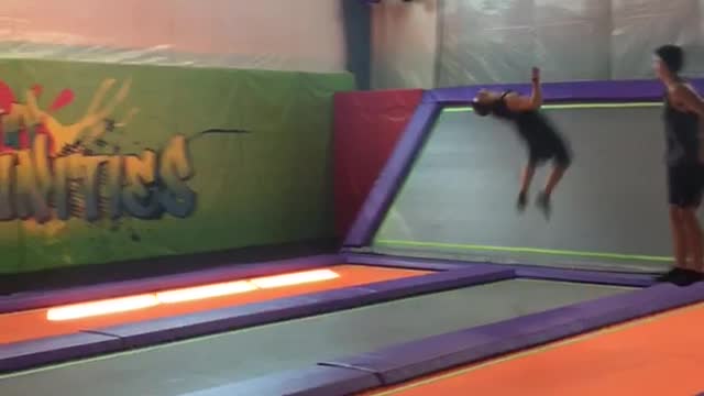 Guy multiple back flips on orange and purple trampoline