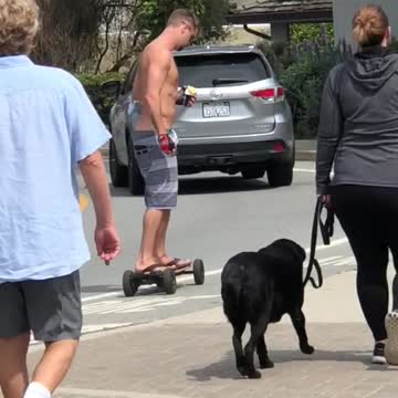 Shirtless guy rides a motorized skateboard on side street