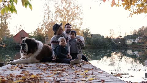 Happy family with their big dog at sunset sit near the lake on an autumn day