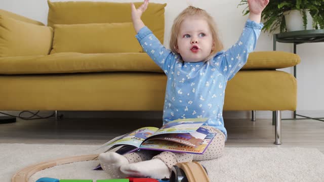 A little girl with a book on her lap flopping her hands