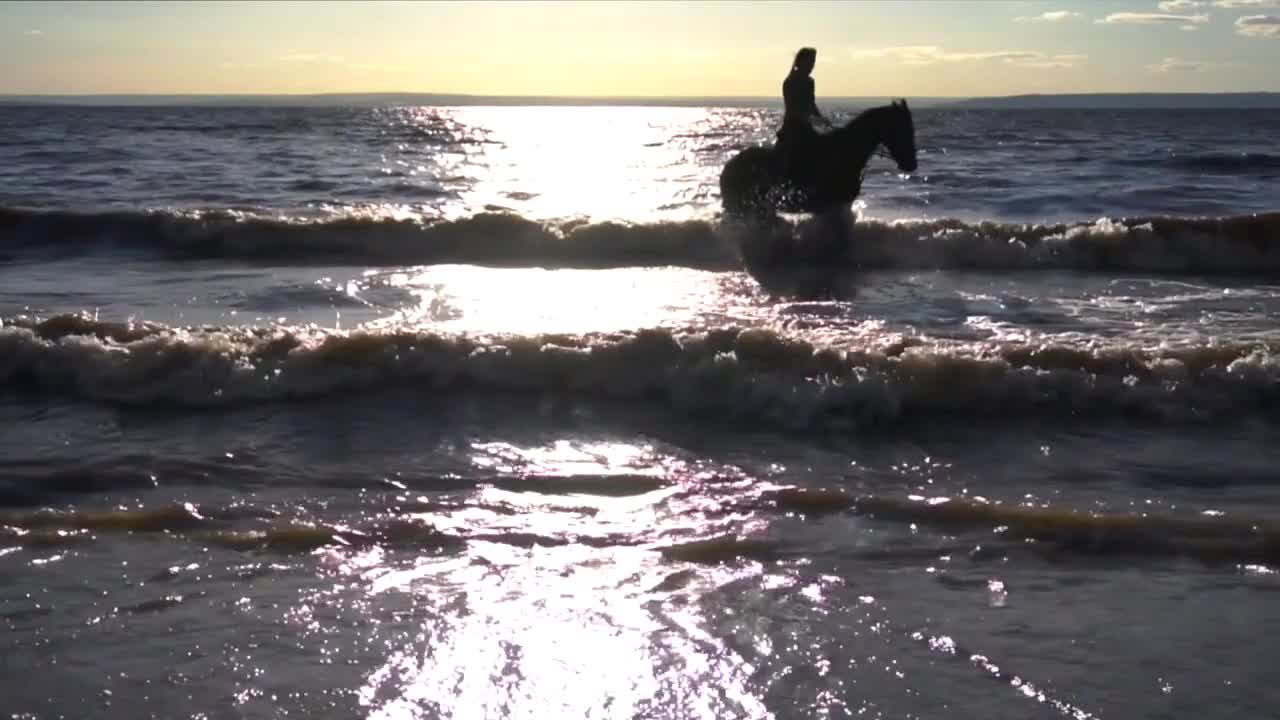 Woman riding on horse at river beach in water sunset light