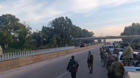 A convoy of the Russian Armed Forces passes by the HTS militants in Tartus.