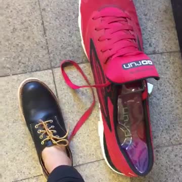 Man with black shoe compares foot to red tennis shoe