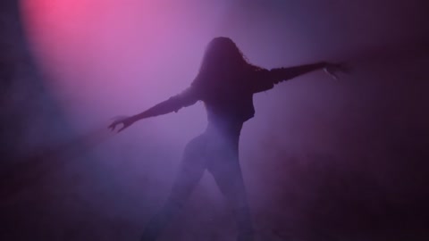 Young woman dancing under a cloud of smoke and a purple light