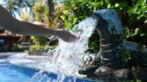 Hand playing with water flow from little turtle fountain