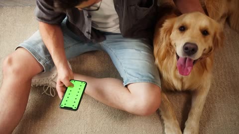 Young man in glasses petting golden retriever sitting on floor in living room