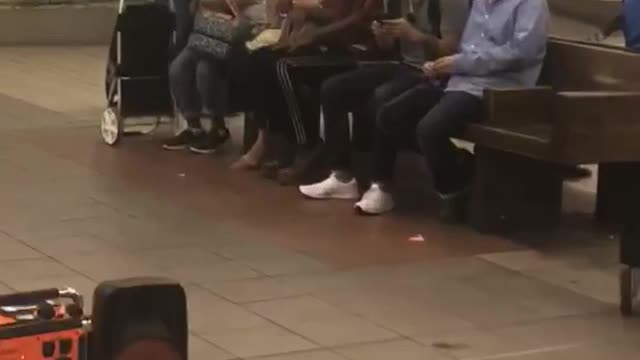 Guy red shirt black hat dancing sits between people subway bench