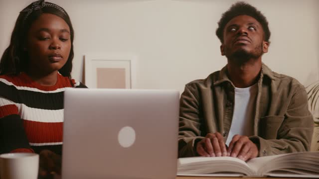 Blind Man Reading Braille Book Beside Woman Using Laptop