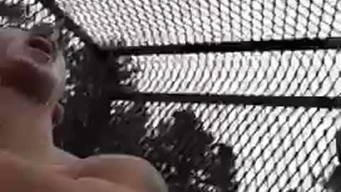 Guy sits on top of tractor and pours beer into shirtless guys mouth
