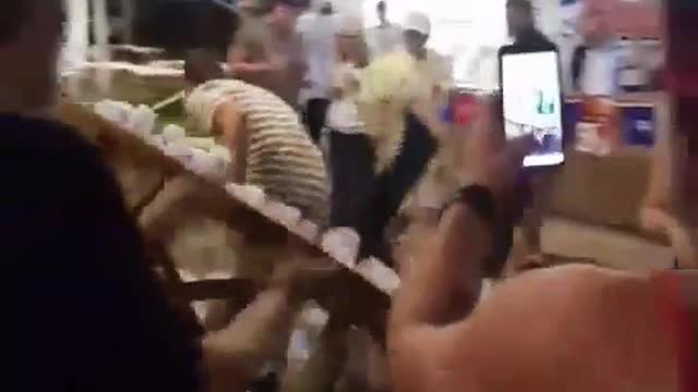 Stripe shirt guy and blue shirt guy knock over tower of clear cups on round wooden table