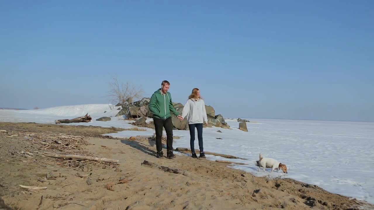 young couple walking on the beach with the dog. spring beach with snow